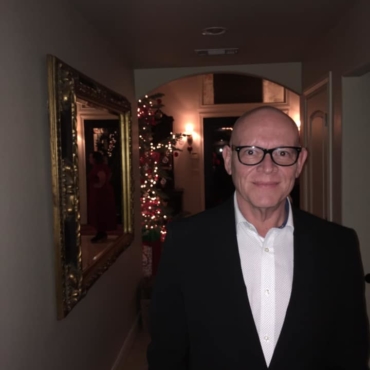 Man with glasses and suit smiling with Christmas tree behind him