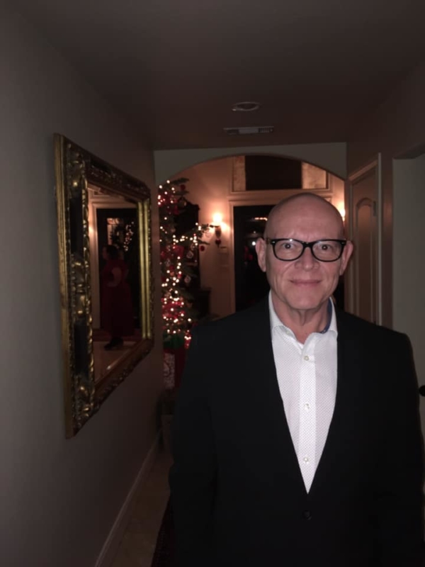 Man with glasses and suit smiling with Christmas tree behind him