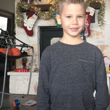 Boy in grey long sleeve smiling with Christmas decor in house
