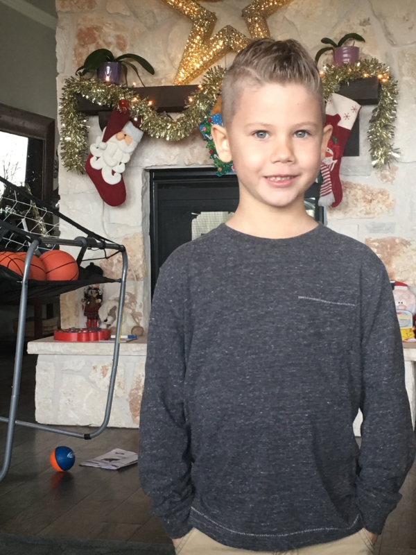 Boy in grey long sleeve smiling with Christmas decor in house