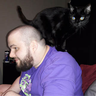 Man in purple shirt looking away from the camera with a black cat on his back