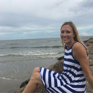 Woman in white and blue striped blouse smiling at the ocean on a rock