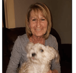 Woman in grey shirt smiling with white furred dog