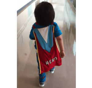Younger child in blue shirt and hero cape walking away