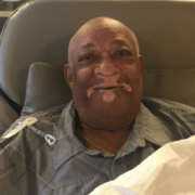 Man in grey shirt grinning while sitting in chair