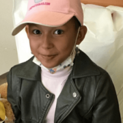 Child in pink hat and face mask over chin with black leather jacket