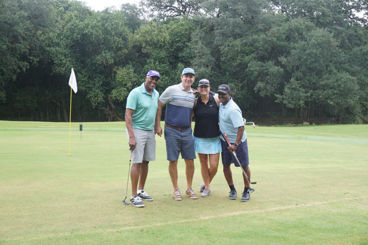 three men and a woman standing together smiling in a golf course