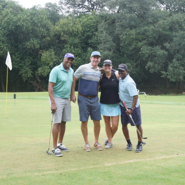 three men and a woman standing together smiling in a golf course