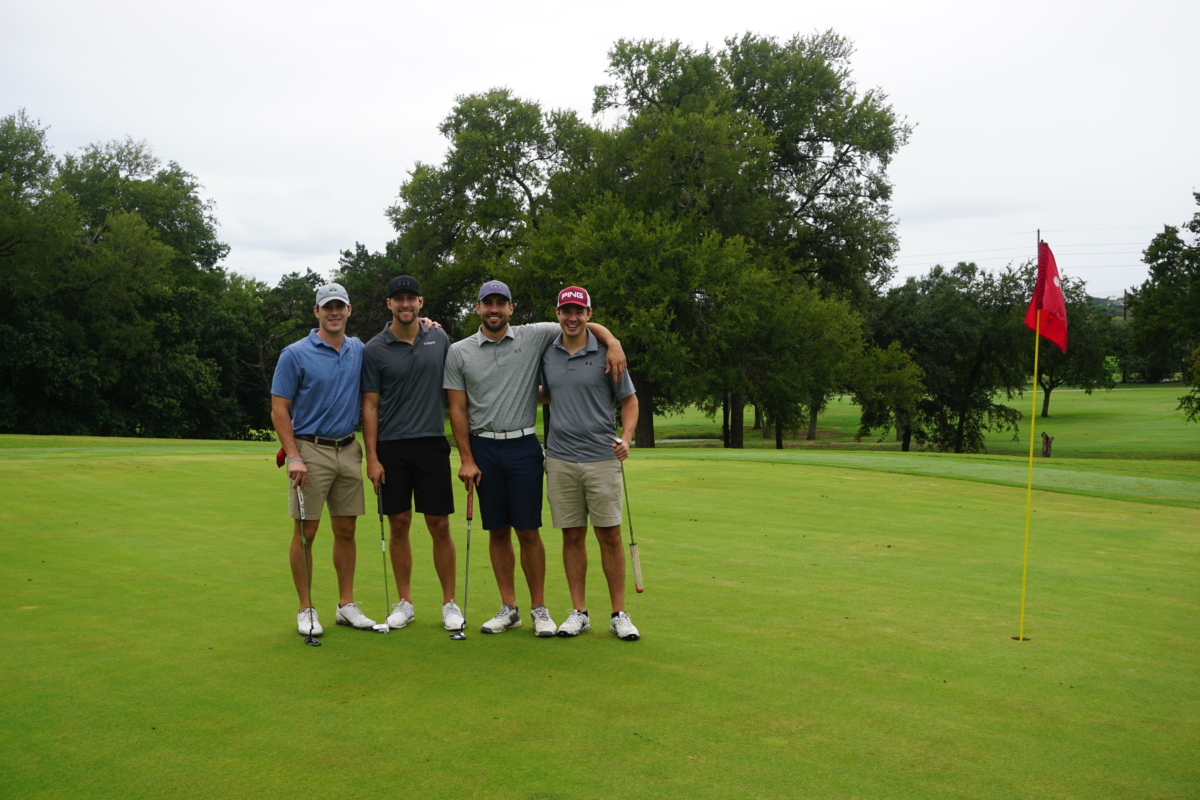 Four men standing together in a golf course holding golf clubs