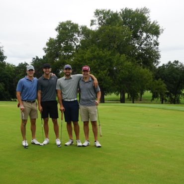 Four men standing together in a golf course holding golf clubs