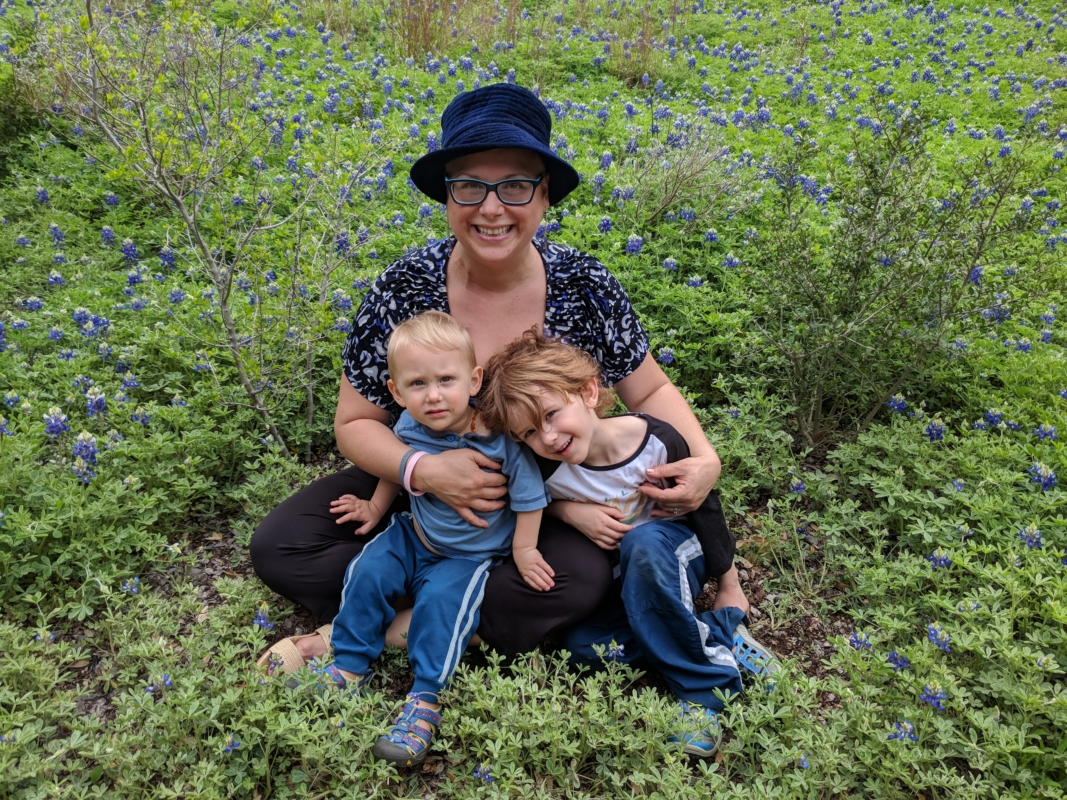 Woman and two boys in blue sitting in a bluebonnet field