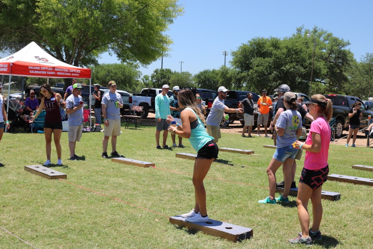 Community outdoor event with several people playing cornhole