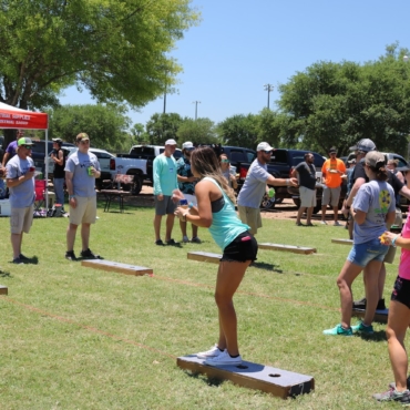 Community outdoor event with several people playing cornhole