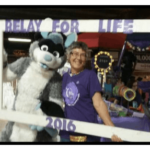 Woman with glasses and purple shirt posing with animal mascot at a Relay for Life event