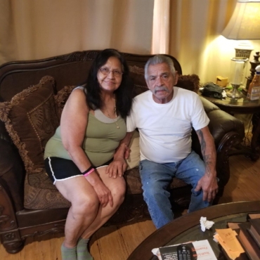 Woman in green with man in white shirt sitting on couch