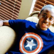 Boy in Captain America t-shirt smiling while sitting in chair