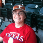 Woman in Texas Rangers shirt and UT Austin hat sitting in a baseball stadium seat