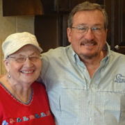 Man in blue button down shirt and woman in red shirt with white bucket hat smiling at the camera