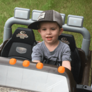 Boy with a cap on and grey shirt driving a toy car