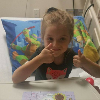 Girl in hospital bed with puzzle giving two thumbs up