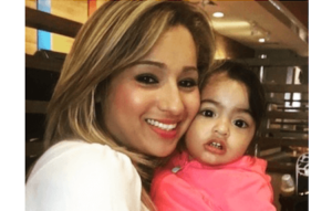 Woman in white and lipstick holding child in pink hoodie