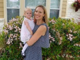 Woman in blue blouse holding girl in all white in front of bushes