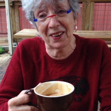 Woman with red and blue glasses smiling with a latte