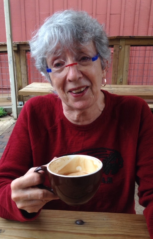 Woman with red and blue glasses smiling with a latte