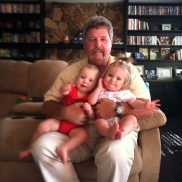 Man sitting down on a couch holding two babies in his arms