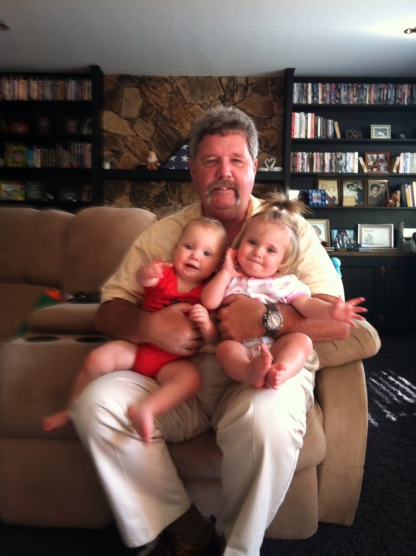 Man sitting down on a couch holding two babies in his arms